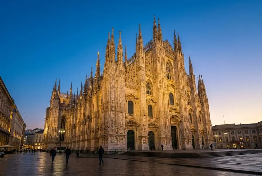 Illuminated Gothic facade of Milan Cathedral (Duomo di Milano) viewed from Piazza del Duomo with a warm winter sunset glow.