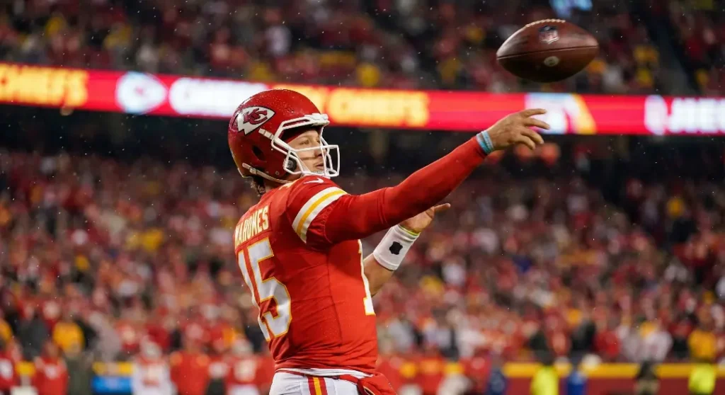 Kansas City Chiefs quarterback Patrick Mahomes executing a behind-the-back throw during a live NFL night game, displaying elite playmaking ability.