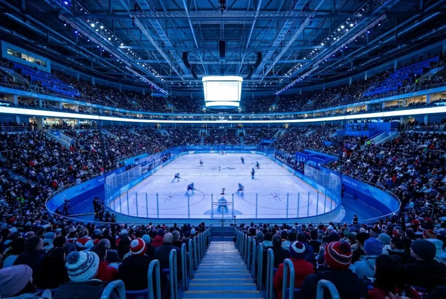 Wide angle view of a modern ice hockey arena with an illuminated rink and packed spectator stands during a Winter Olympics game.
