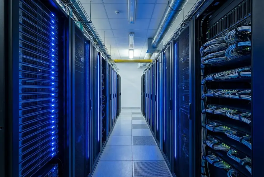 Rows of high-performance computer server racks with glowing blue LED status lights and cabling in a secure data center facility.