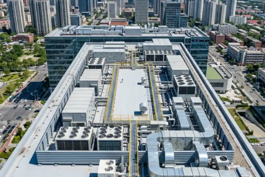 An expansive commercial rooftop HVAC system featuring multiple industrial chiller units, large silver ductwork, and exhaust fans on top of a modern urban office building.