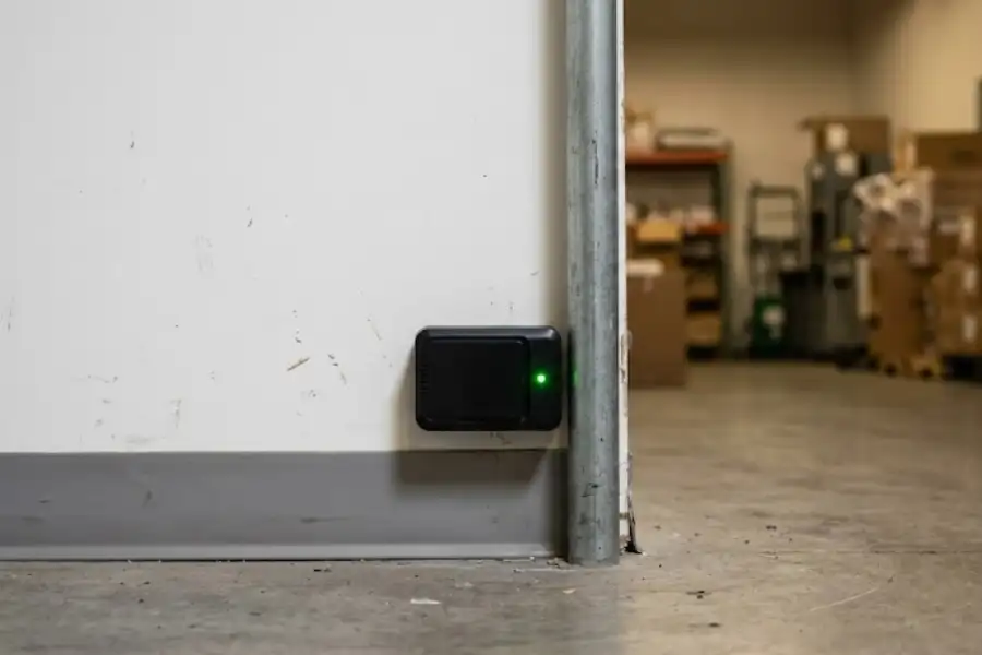 Close-up of a black smart pest monitoring sensor with a green LED light installed on a commercial wall by professional pest control services.