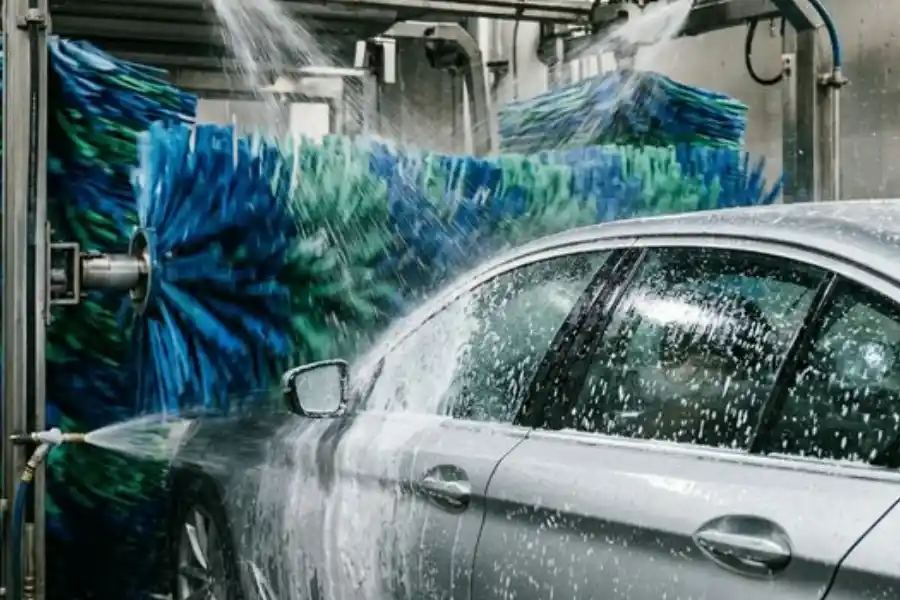 Close-up of soft blue and green rotating brushes perfectly contoured to the side of a silver sedan in a car wash tunnel
