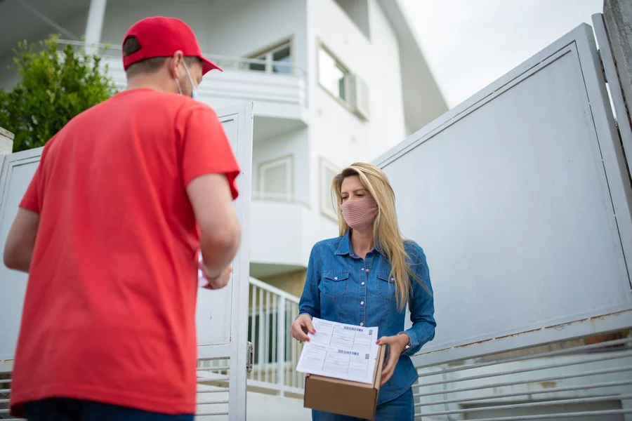 Visitor At The Door Delivery courier carrying a parcel to a house entrance past a doorbell camera