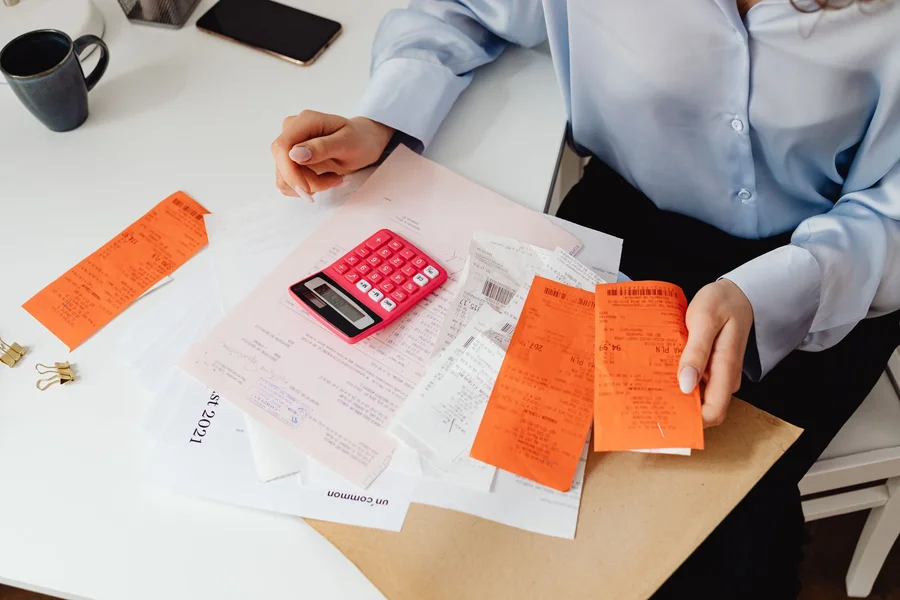 Person calculating shared household bills with a calculator and paperwork at a desk