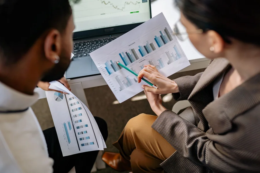 Reviewing consultant results Two people reviewing printed marketing charts beside a laptop at a desk