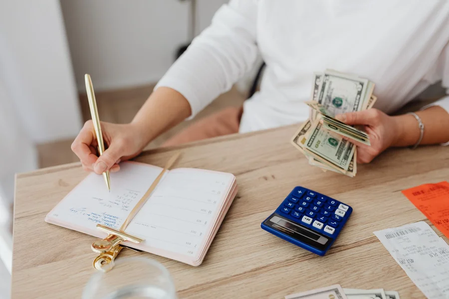 Person tracking handmade business costs with a notebook, receipts and calculator