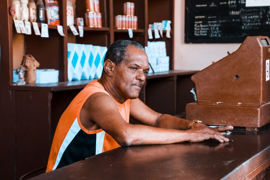 Older worker at a shop counter beside a cash register during a part-time shift