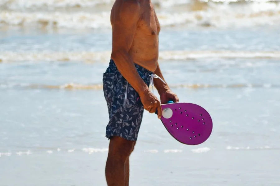 Player holding a solid beach racket with drilled holes beside the sea