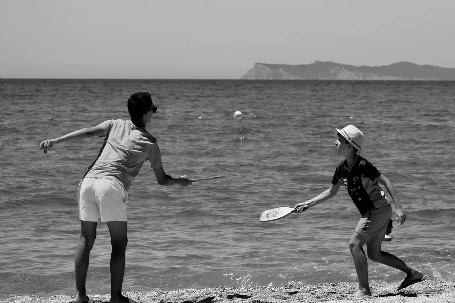 Two people rallying with solid beach rackets at the water’s edge