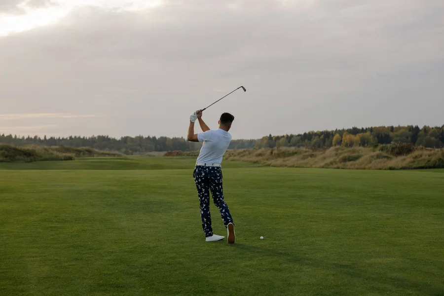 Cold-weather golf layering Golfer swinging on an autumn fairway under an overcast sky