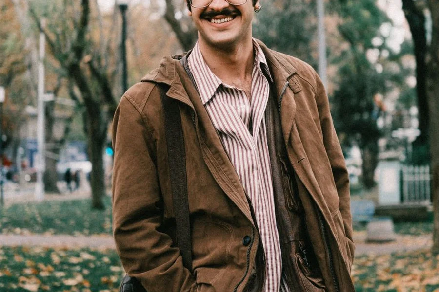 Man wearing an open brown utility jacket over a striped shirt outdoors